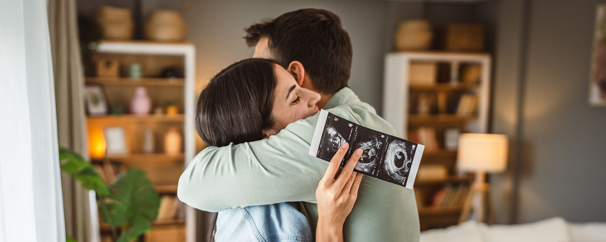 Happy,Pregnant,Woman,With,Hug,Her,Husband,And,Watch,Ultrasound Happy pregnant woman with hug her husband and watch ultrasound photo of baby