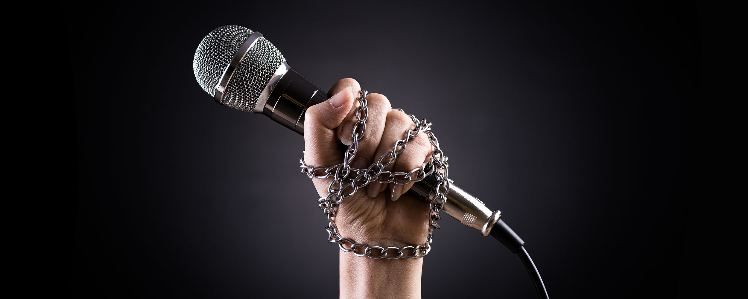 World press freedom day concept. Hand holding a microphone with chain on dark background, symbol of press freedom or speech freedom.